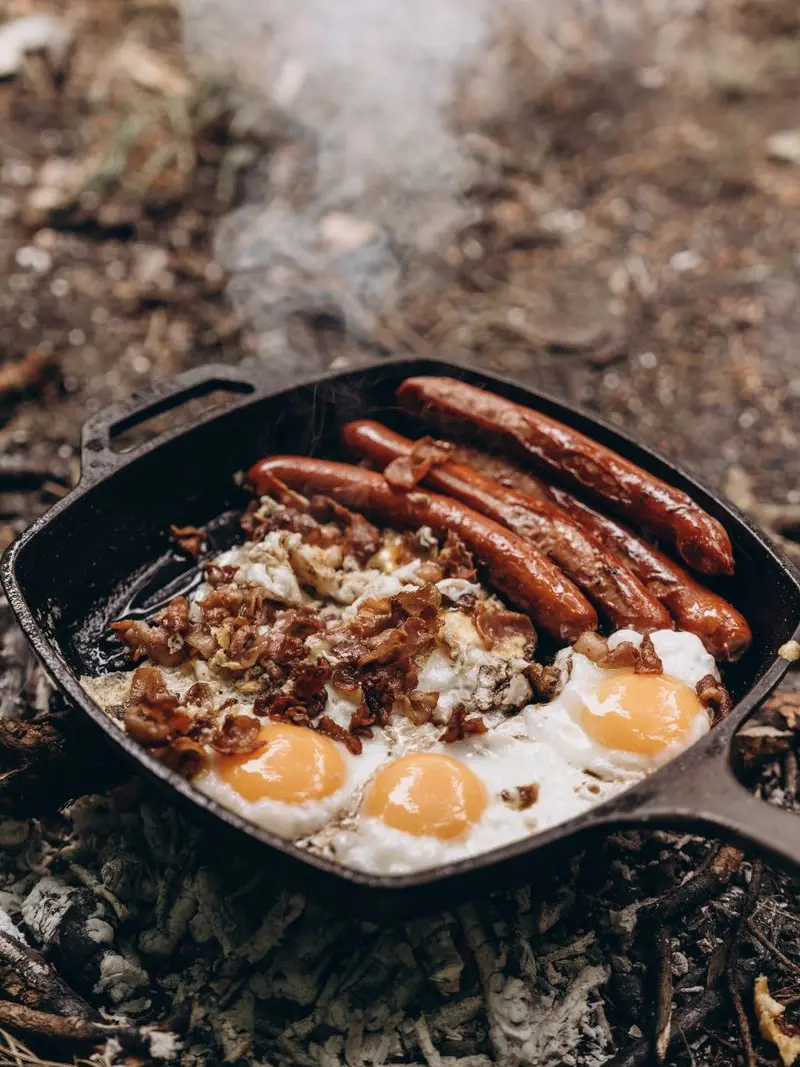 Eggs, sausages and bacon cooking in a cast-iron skillet over a campfire