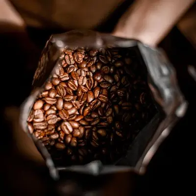 Hands holding an open bag of whole coffee beans