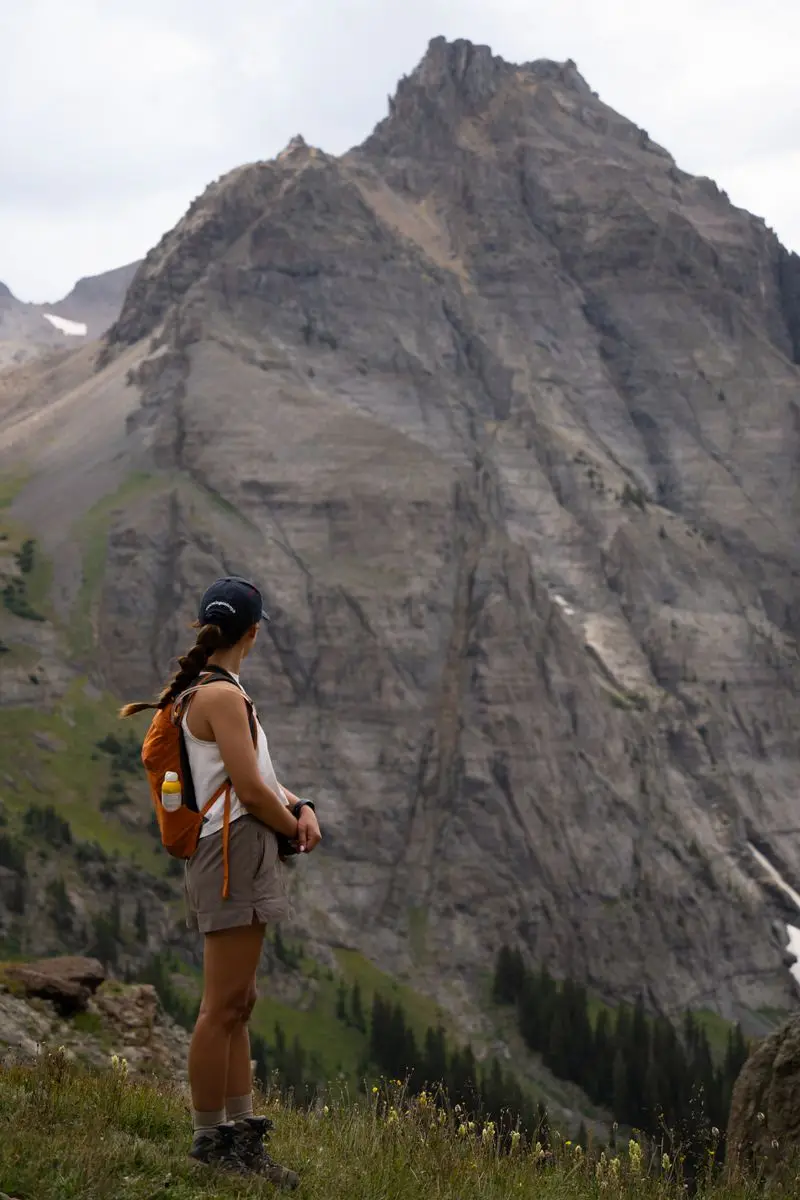 A hiker with a small backpack looking up at a tall rocky mountain peak