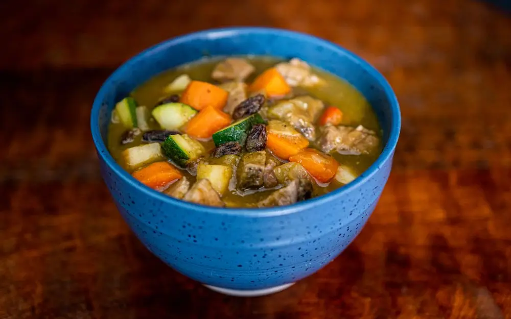 A blue bowl of vegetable stew on a wooden table