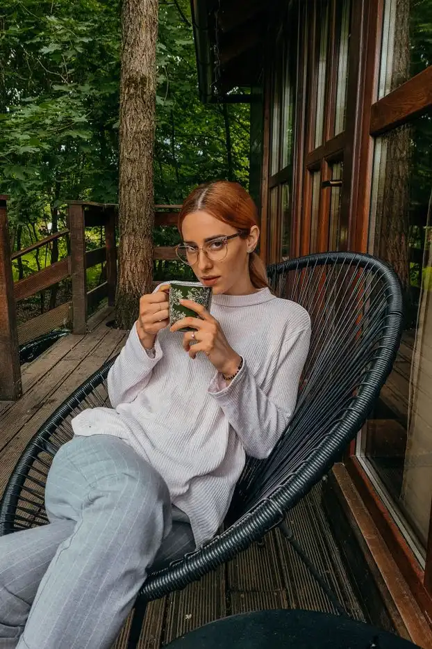 A woman with a mug of tea sitting on a wooden cabin deck in the forest