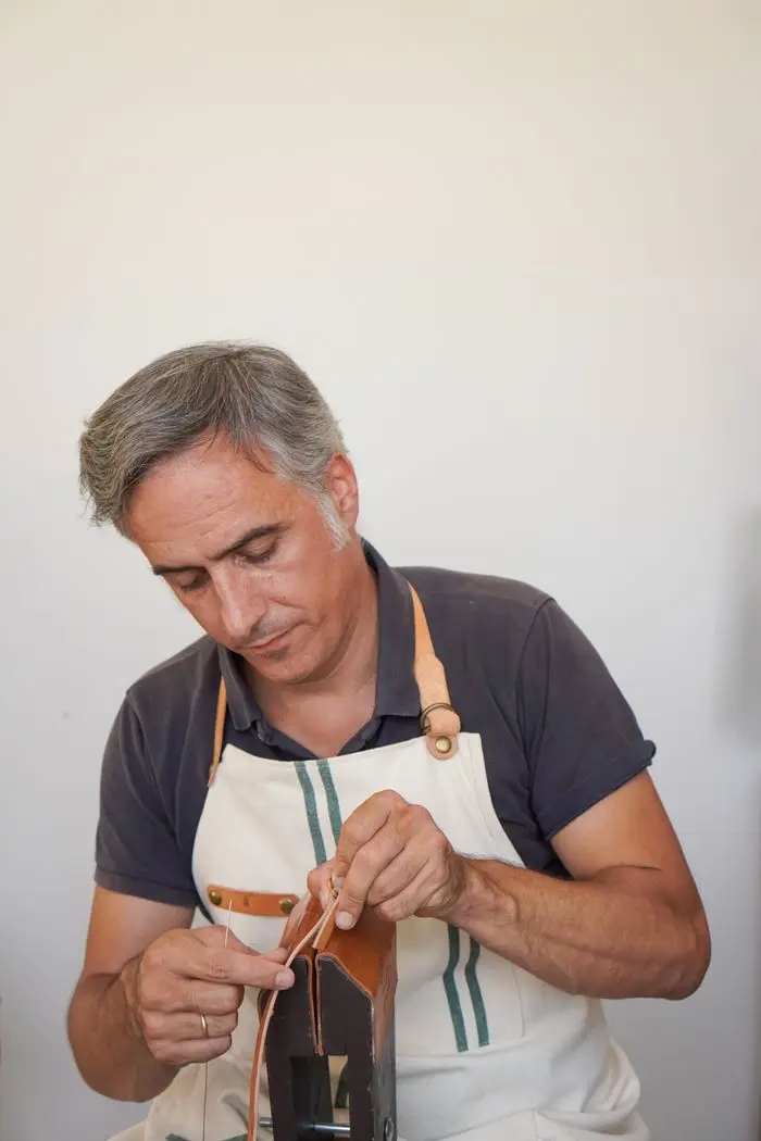 A craftsman in an apron hand-stitching a piece of leather