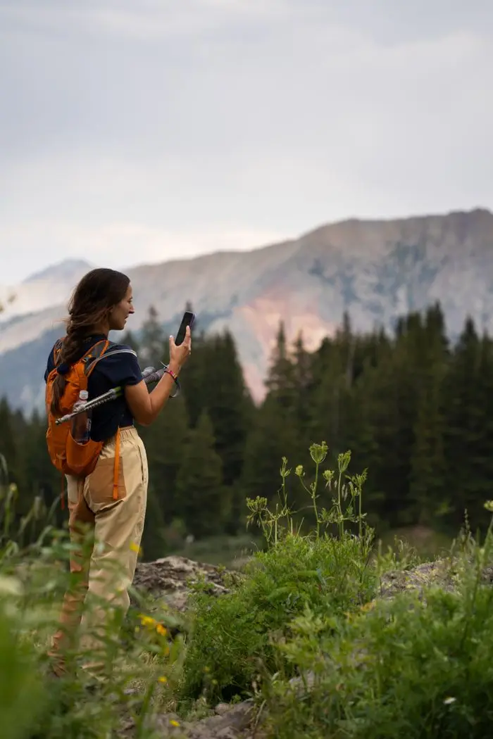 A hiker with a backpack taking a photo of the mountains from a pine meadow