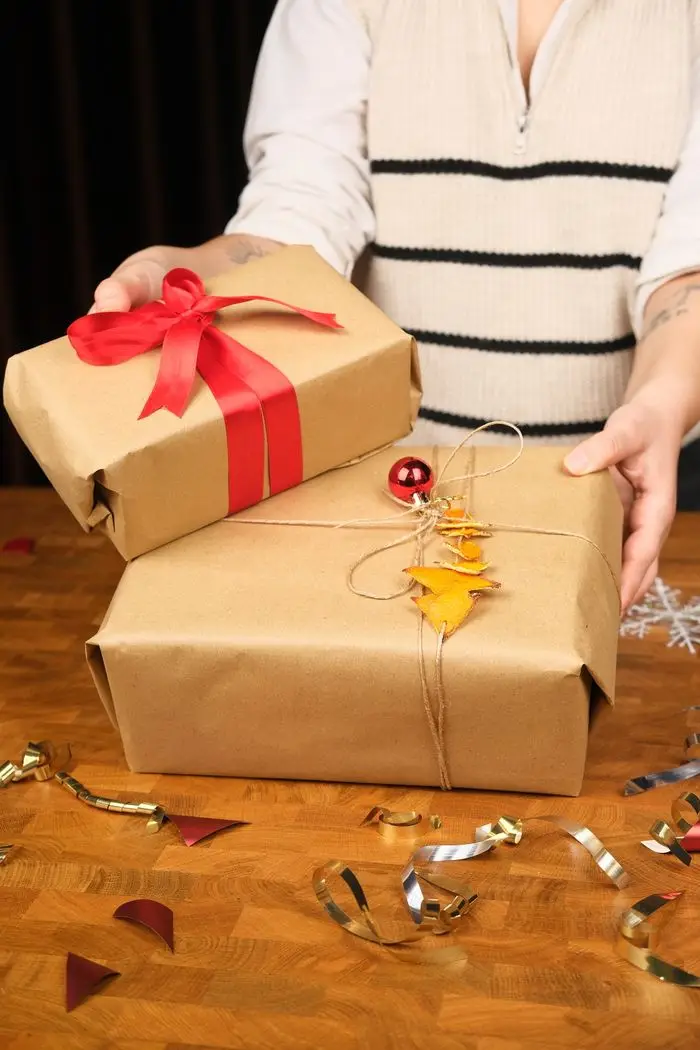 Hands setting down presents wrapped in kraft paper with red ribbon